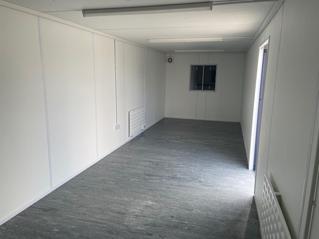 Inside of a portable cabin. The room has white walls and two radiators, it is empty.
