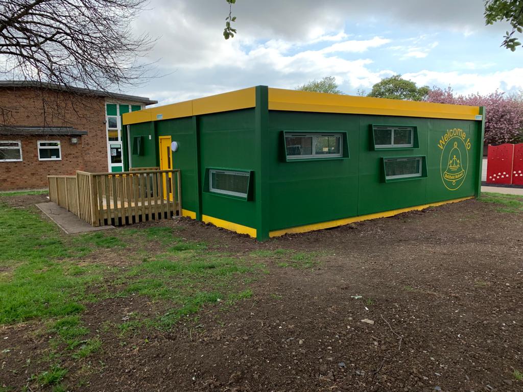 Green & yellow modular classroom building with wooden ramp leading to the entrance.