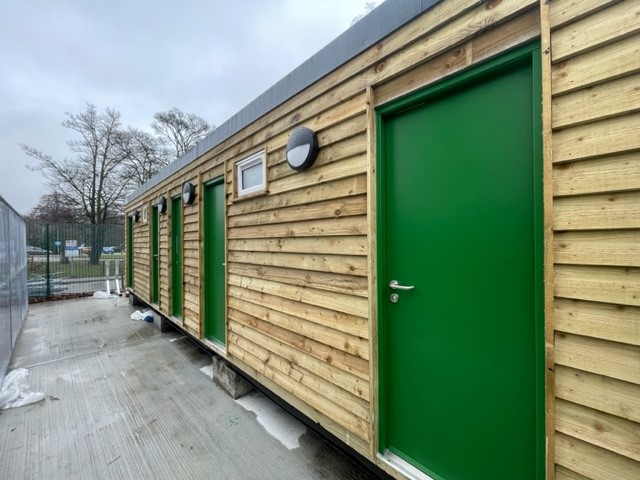 Portable cabin with external timber cladding and multiple green doors.