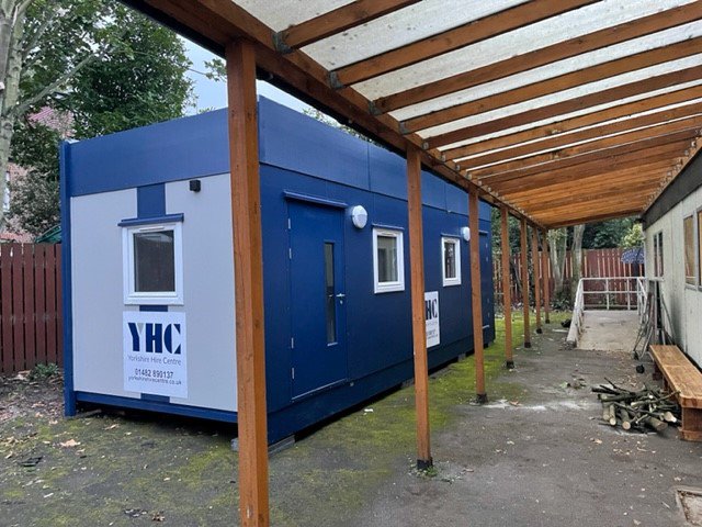 Portable cabin installed on site next to existing modular building.